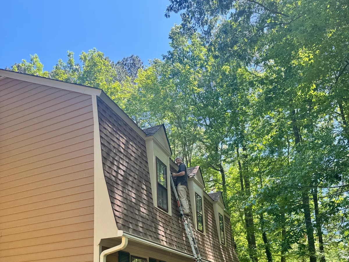 Justin on a ladder inspecting the roof and dormers of a Central Virginia home