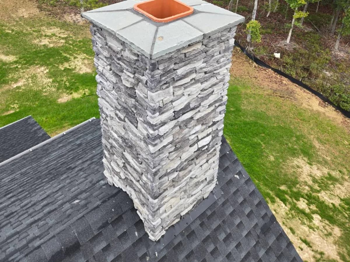 Stone chimney with a fresh crown and clay flue, seen from above the roof