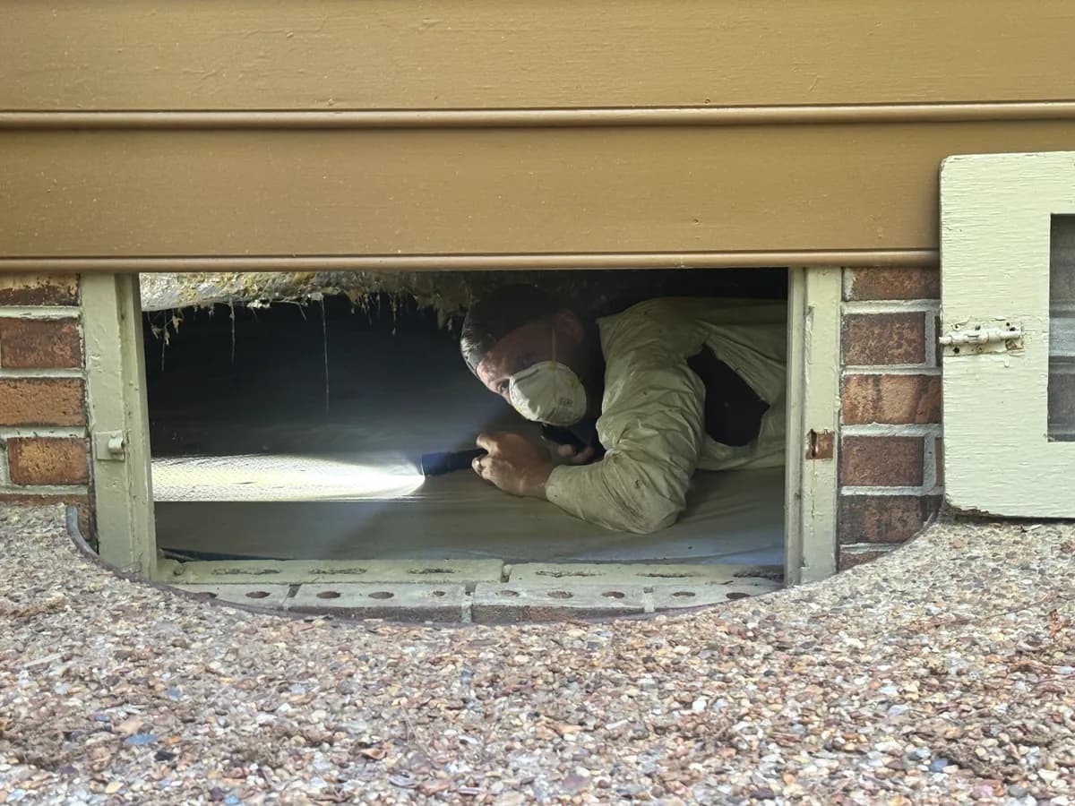 Justin entering a crawlspace access hatch with a flashlight and respirator
