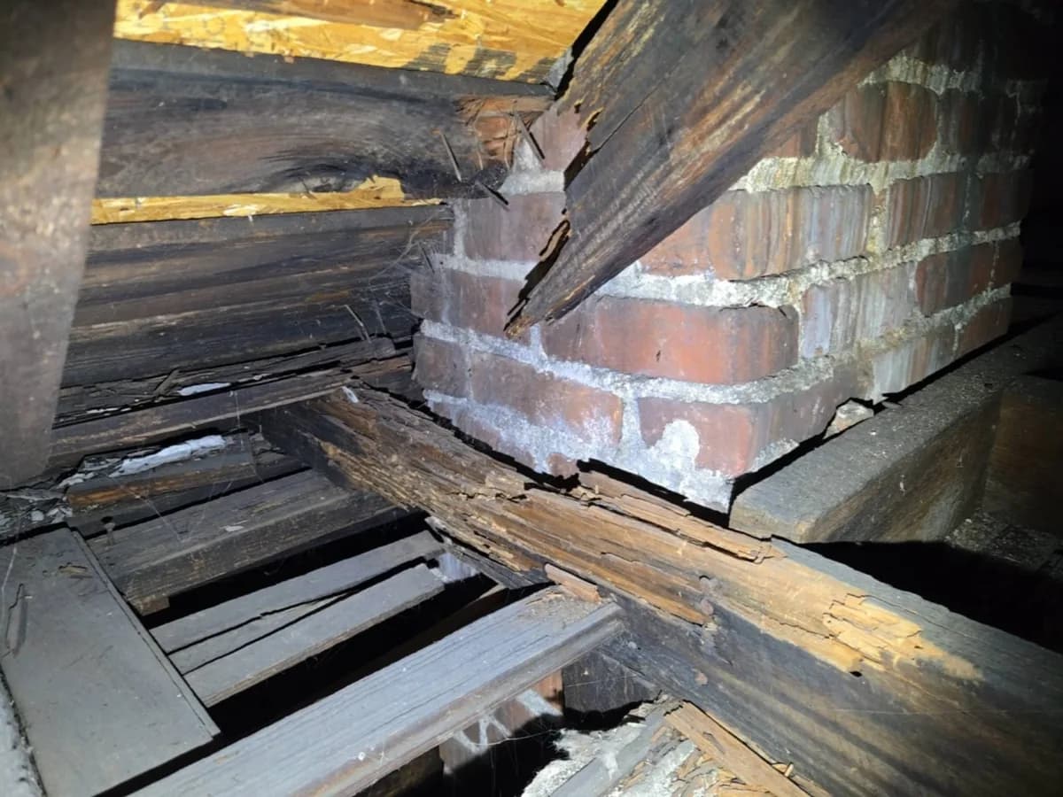 Damaged roof framing and wood rot around a brick chimney in an attic